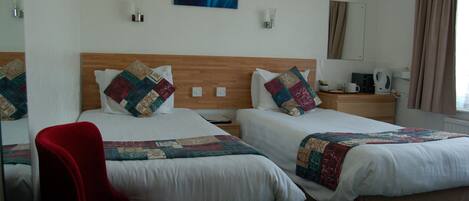 A hotel room with two beds, a red chair, a coffee maker, and a painting on the wall.