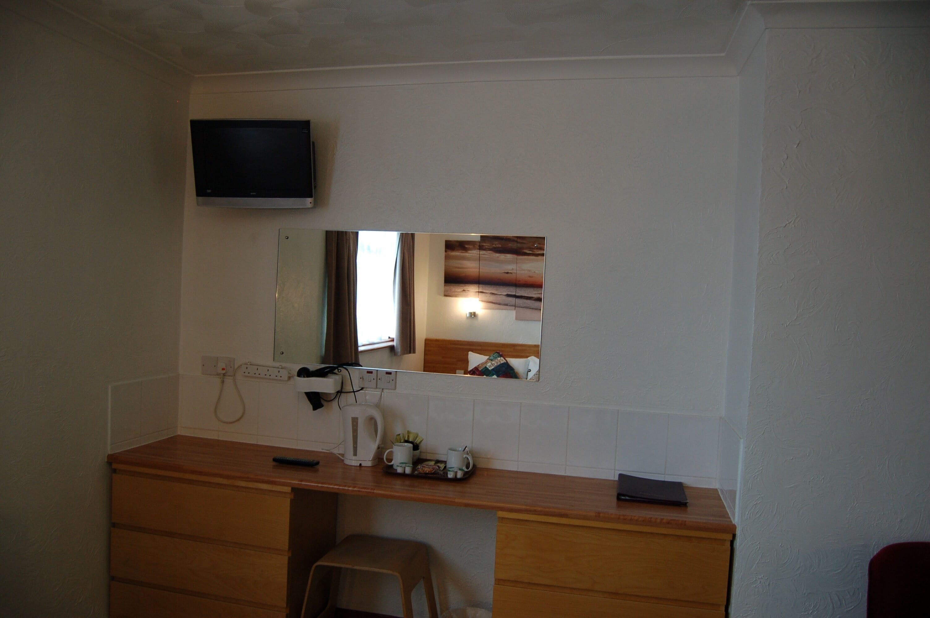 A bathroom with a wooden vanity, a mirror, a television mounted above the mirror, and a towel rack.