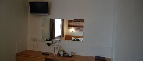 A bathroom with a wooden vanity, a mirror, a television mounted above the mirror, and a towel rack.