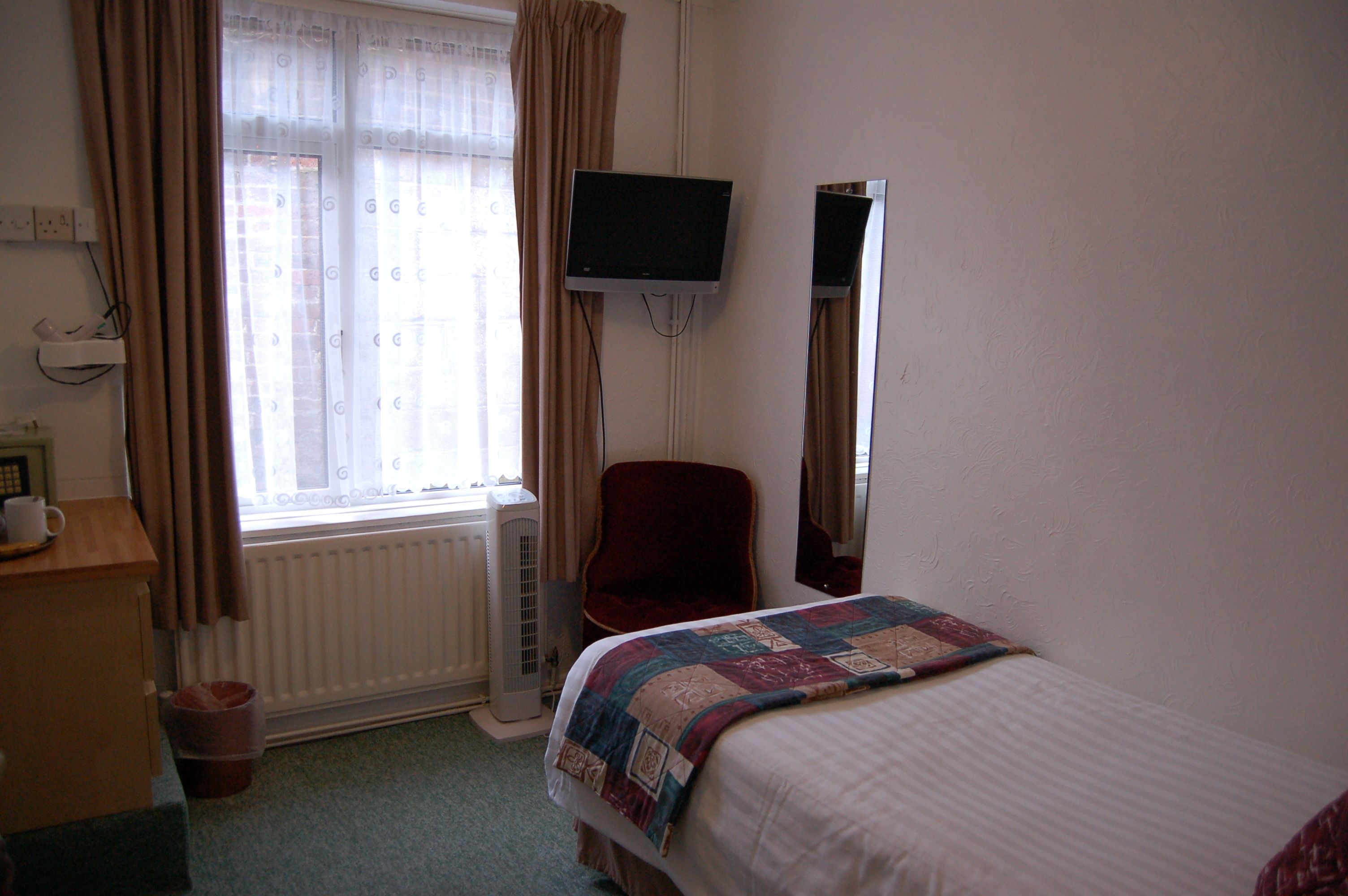 A hotel room with a bed, a chair, a television mounted on the wall, a radiator, and a window with curtains.