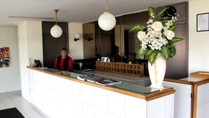 Um balcão de recepção com tampo de vidro, bancada de madeira e um vaso de flores branco.