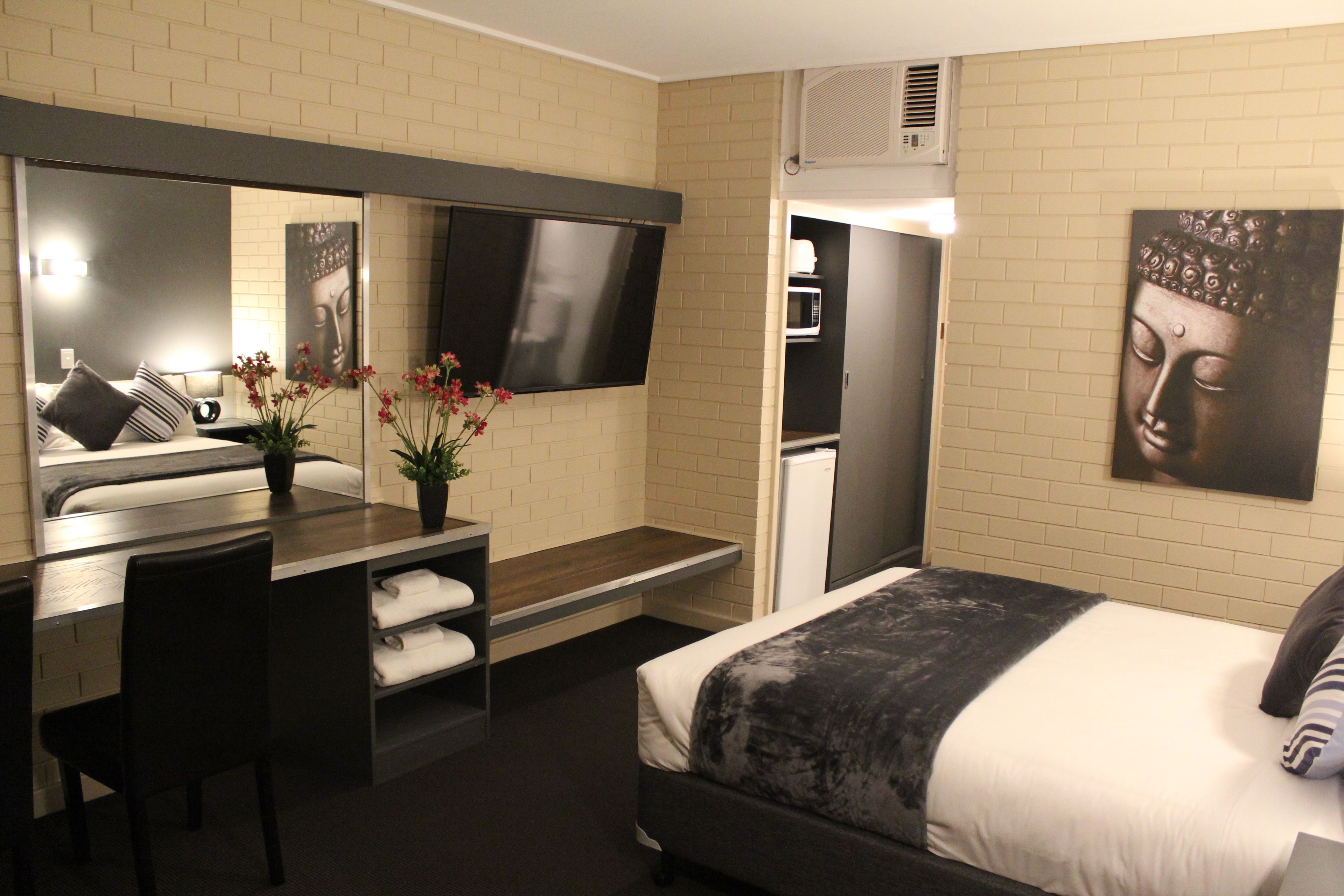 Een hotelkamer met een bed, een bureau met stoel, een flatscreen-tv, een magnetron, en een grote Boeddhabele afkomstig van de muur.