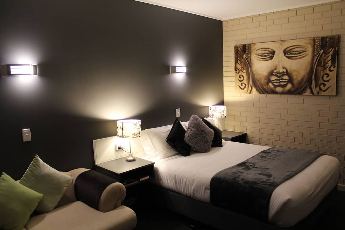 Habitación de hotel con cama, mesita de noche, lámpara y una obra de arte colgada en la pared.