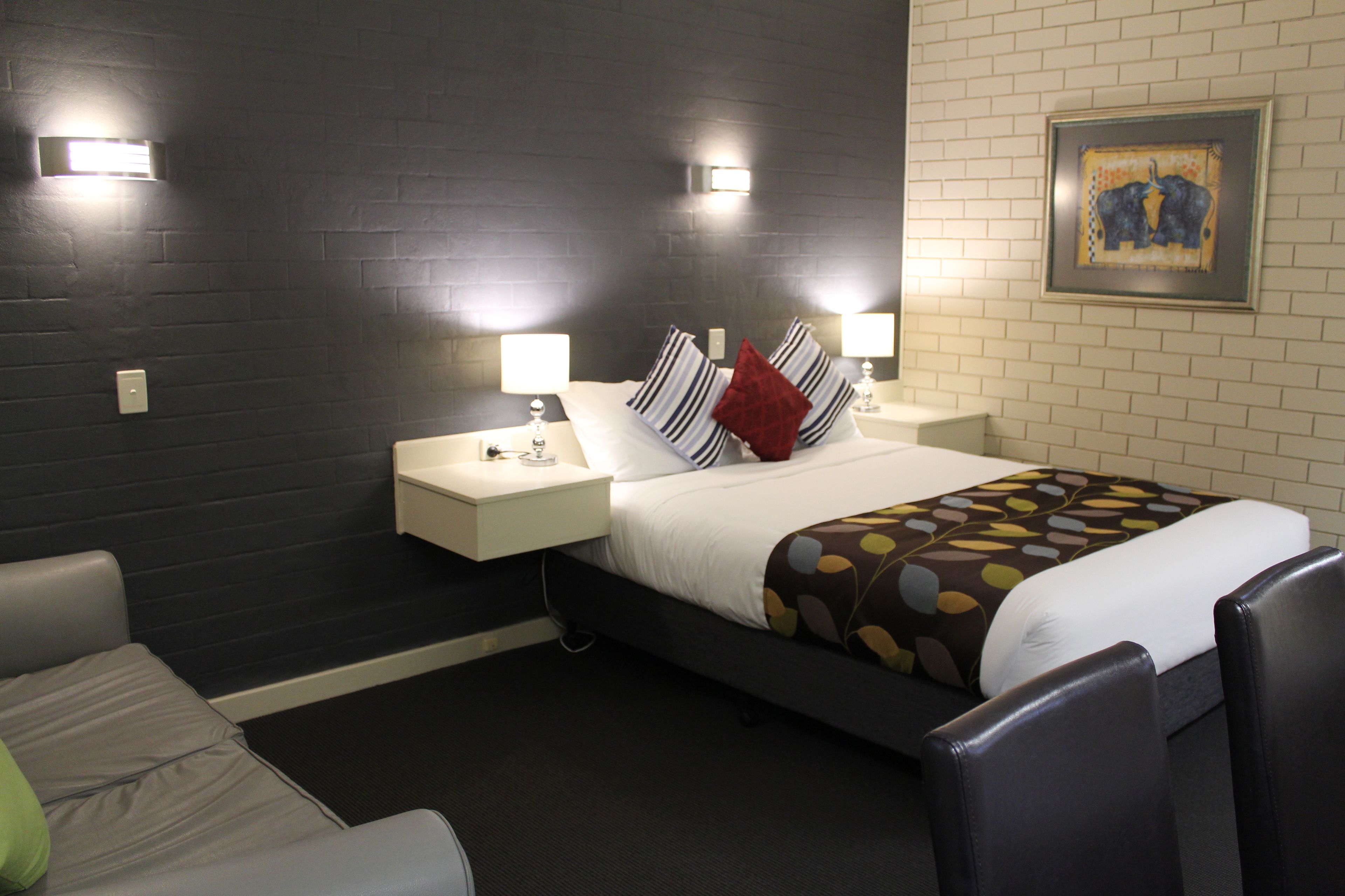 A hotel room with a dark wall, a bed with striped pillows, a patterned throw, and two bedside lamps.