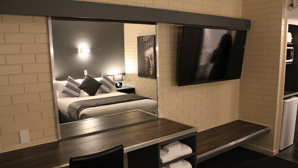 Quarto de hotel com cama, mesa de cabeceira, cadeira e televisão de tela plana na parede.