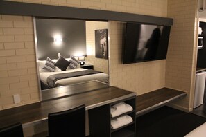 A hotel room with a bed, bedside table, chair, and a flat-screen TV mounted on the wall.