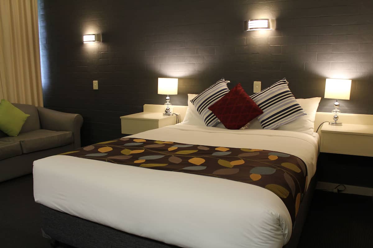 Habitación de hotel con una cama grande, dos mesitas de noche con lámparas, un sofá y una pared de ladrillo oscuro.