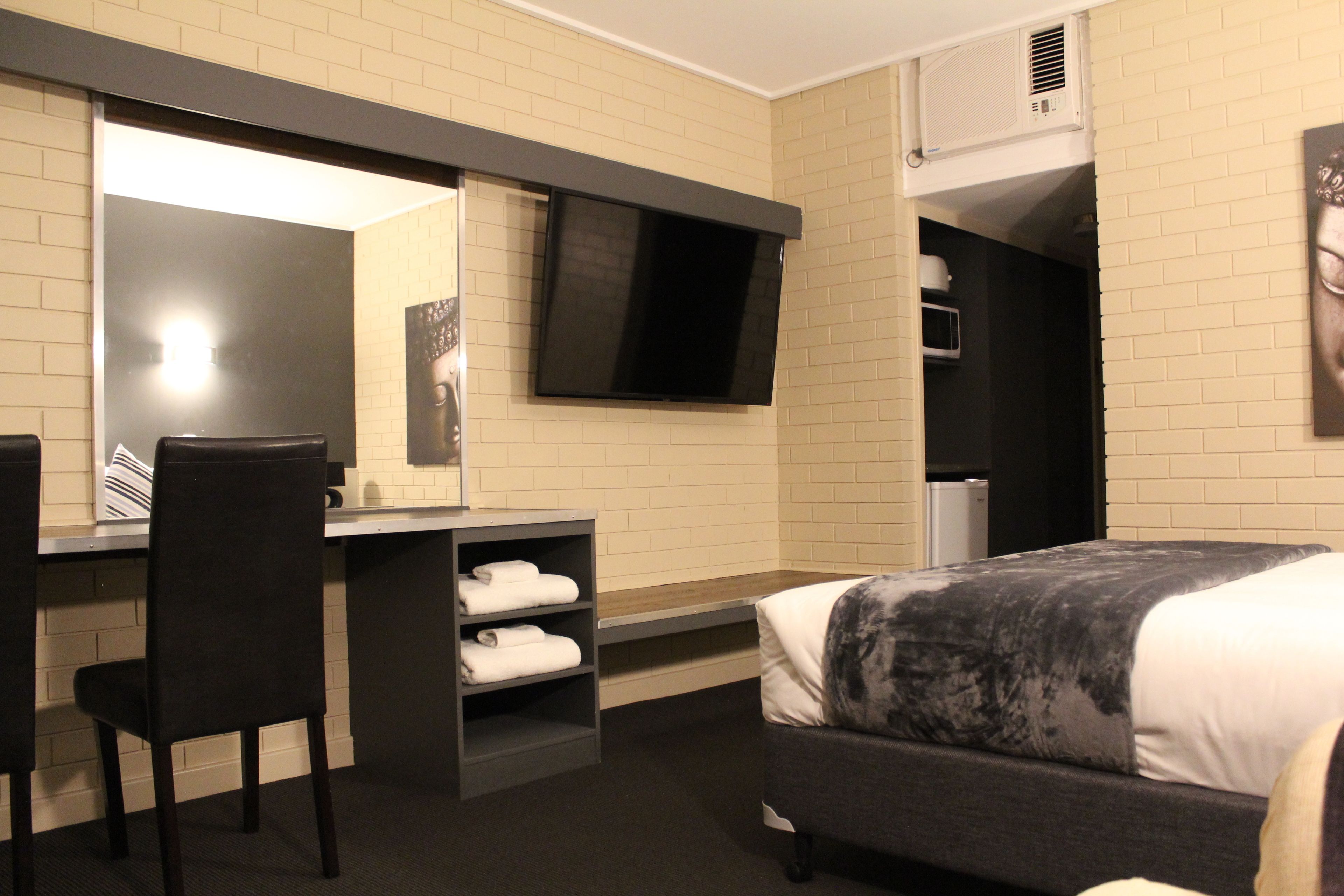 A hotel room with a bed, a desk with a chair, a flat-screen TV, a mirror, and a wardrobe.