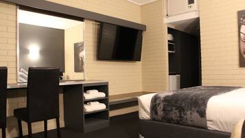A hotel room with a bed, a desk with a chair, a flat-screen TV, a mirror, and a wardrobe.