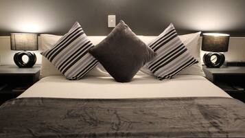A neatly made bed with striped pillows and a dark throw blanket, flanked by two bedside tables with lamps.