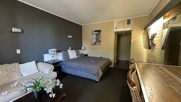 Quarto de hotel moderno com sofá, cama, mesa de madeira e uma pequena planta.