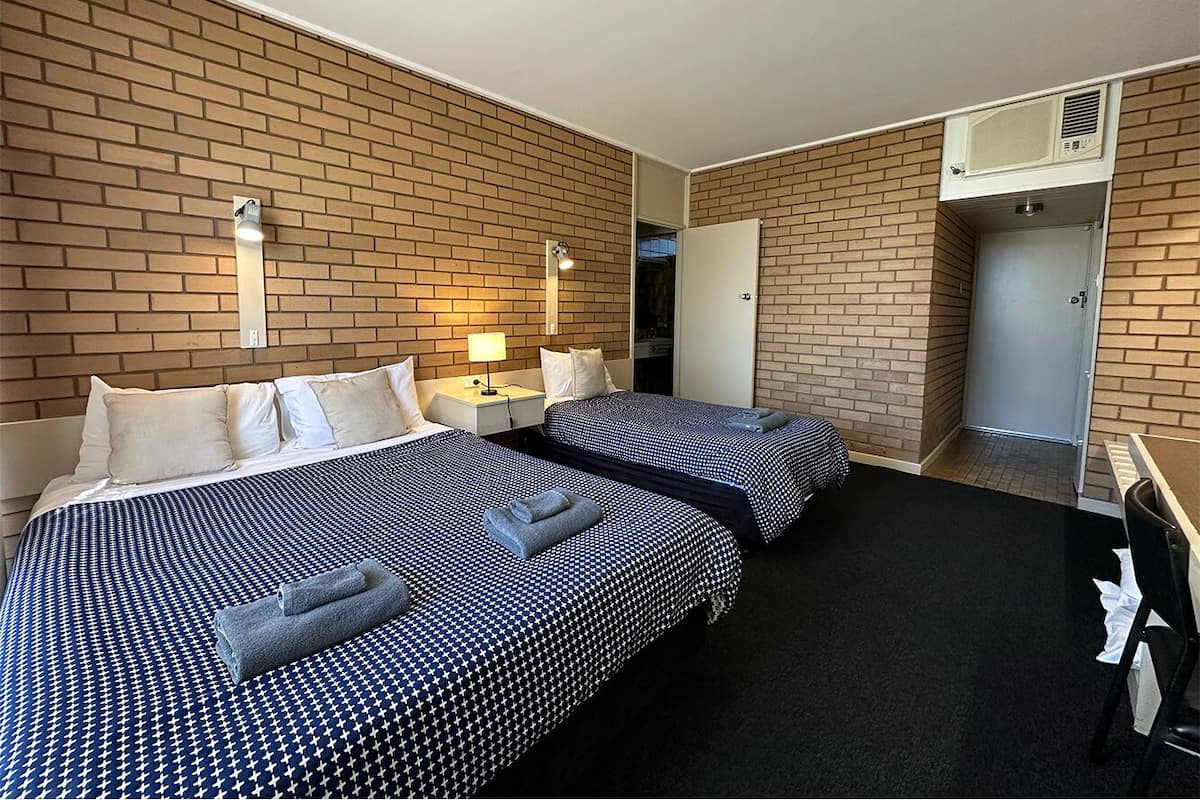 Habitación de hotel con dos camas, un escritorio, una silla, un armario y la puerta del baño.