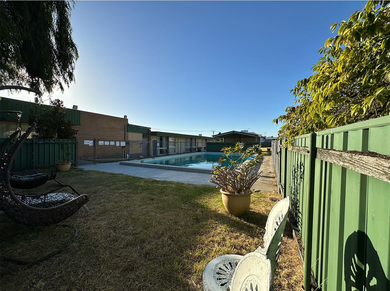 A backyard with a swimming pool, a green fence, and a chair.
