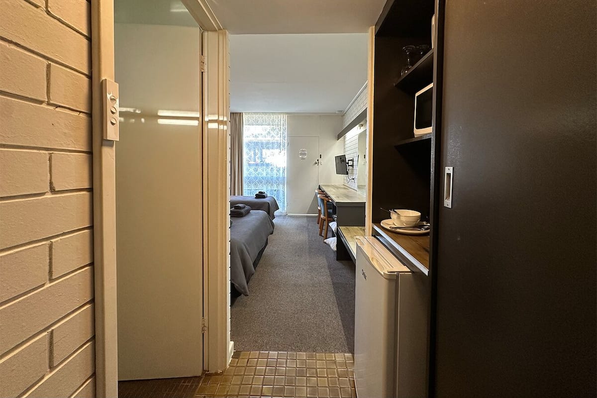 Un pasillo estrecho que conduce a un dormitorio con dos camas, una kitchenette pequeña y un baño con ducha.