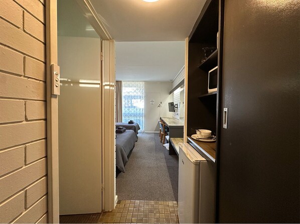 A narrow hallway leading to a bedroom with two beds, a small kitchenette, and a bathroom with a shower.
