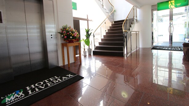 Un vestíbulo de hotel con piso de baldosas brillantes, un ascensor, una escalera y una mesa de recepción con un arreglo floral.