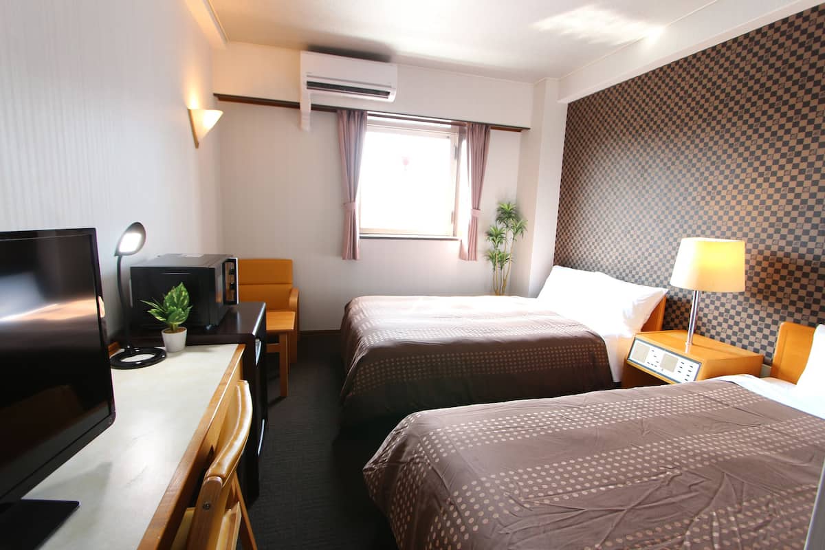 Una habitación de hotel con dos camas, un escritorio con computadora, televisor y lámpara.