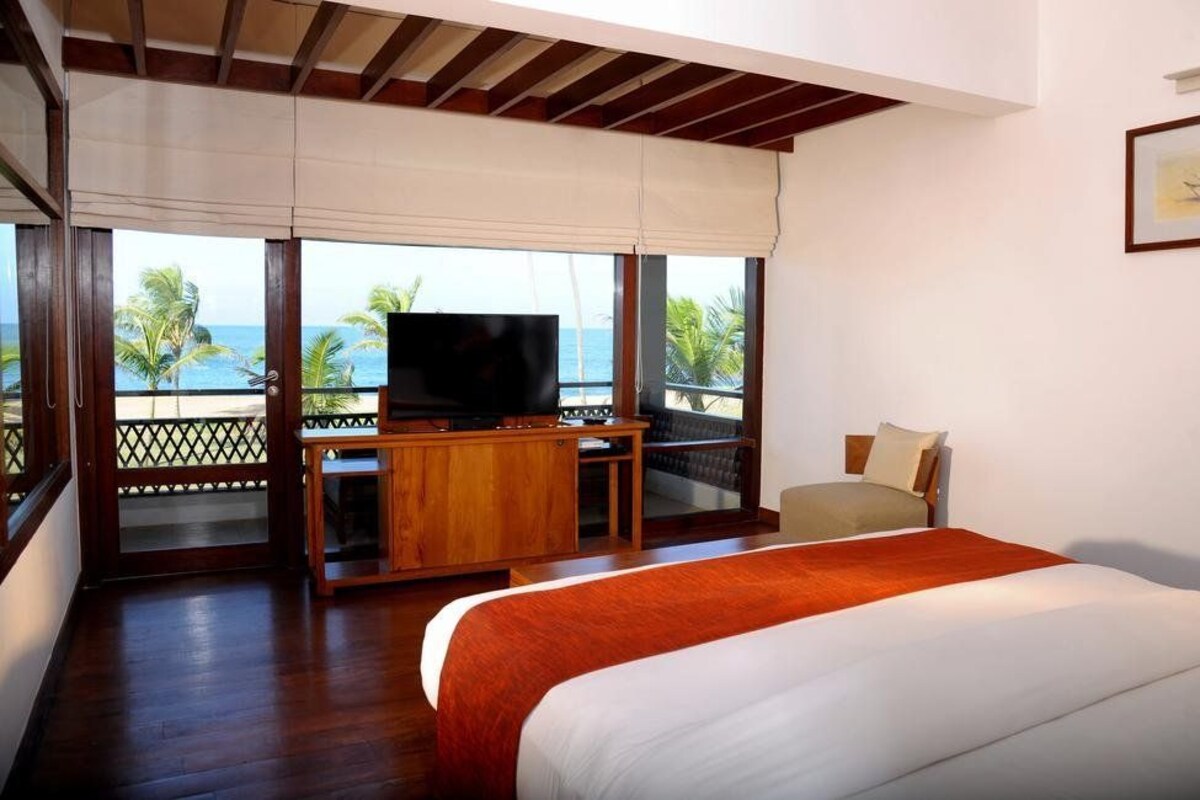 Een hotelkamer met een groot bed, een televisie en een balkon met uitzicht op de oceaan.