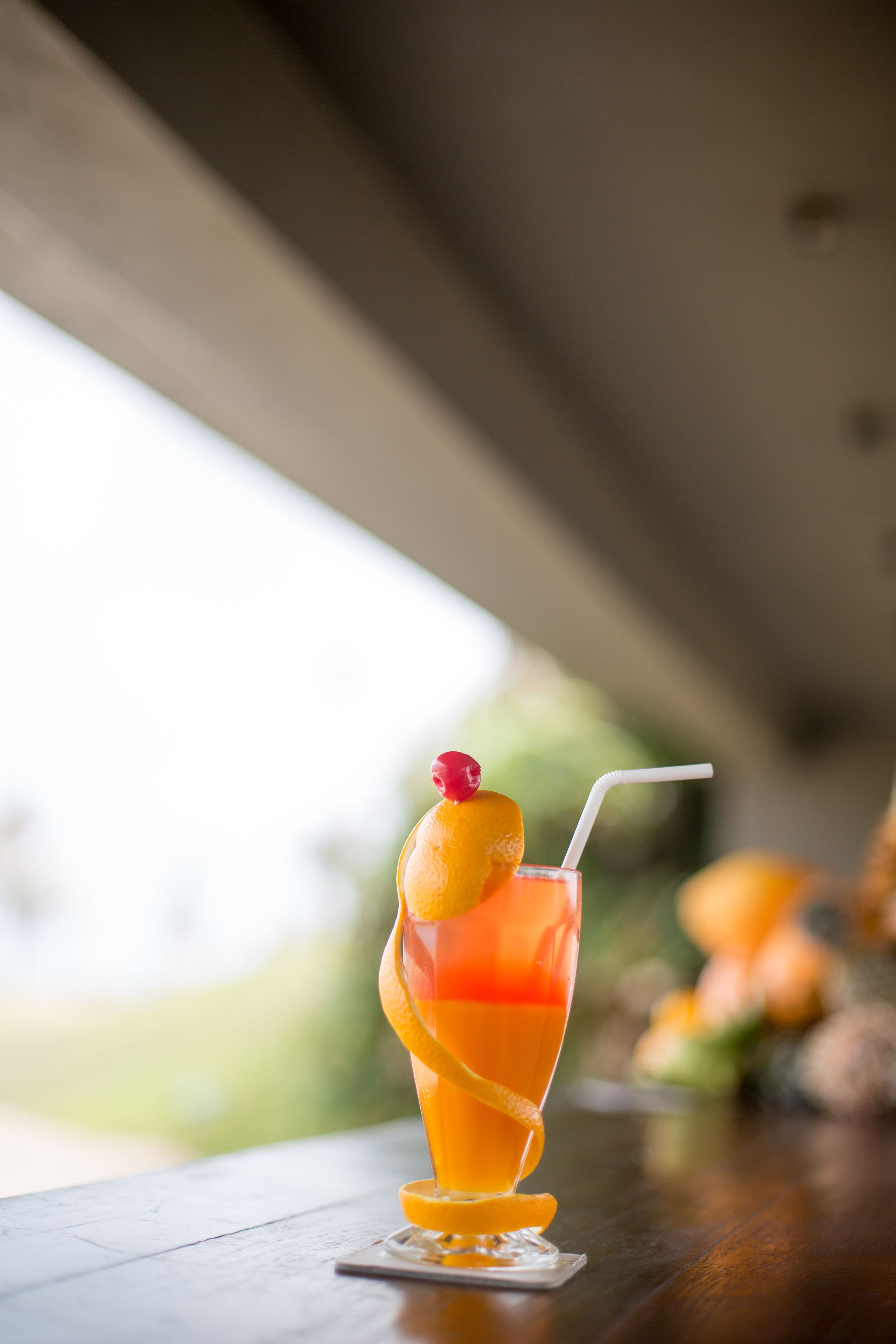 A cocktail with a cherry garnish and a straw, placed on a coaster on a wooden table.