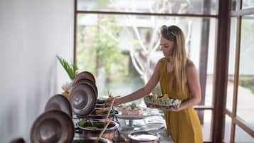 Eine Frau im gelben Kleid serviert Speisen an einem Buffet mit verschiedenen Gerichten und Besteck.
