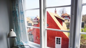 Une pièce dotée d’une grande fenêtre, d’une lampe et offrant une vue sur des maisons aux couleurs vives.