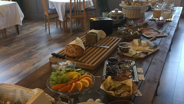 Une longue table à manger, dressée avec divers plats et couverts, entourée de chaises et de fenêtres.