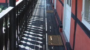 Une passerelle couverte en bois, dotée de rampes noires, un bâtiment rouge avec des ornements blancs et une lanterne noire suspendue au plafond.