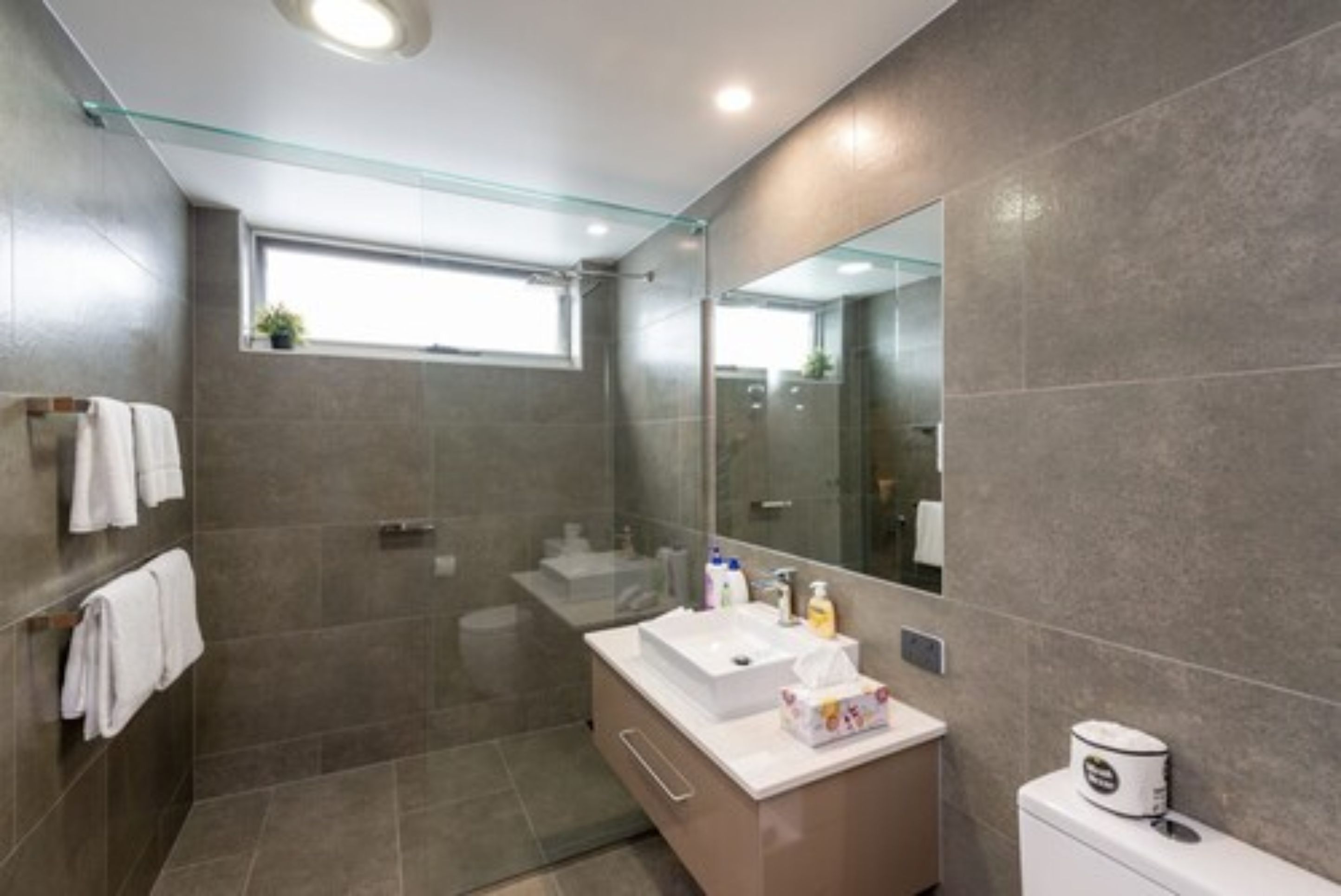 Un baño moderno con cabina de ducha de vidrio, un espejo grande y un lavabo blanco.
