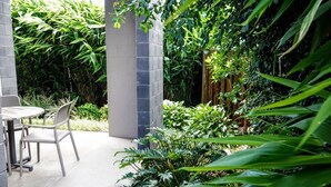 A patio area with a round table and chairs, surrounded by lush greenery and bamboo plants. - Laguna Apartments (Toowoomba)