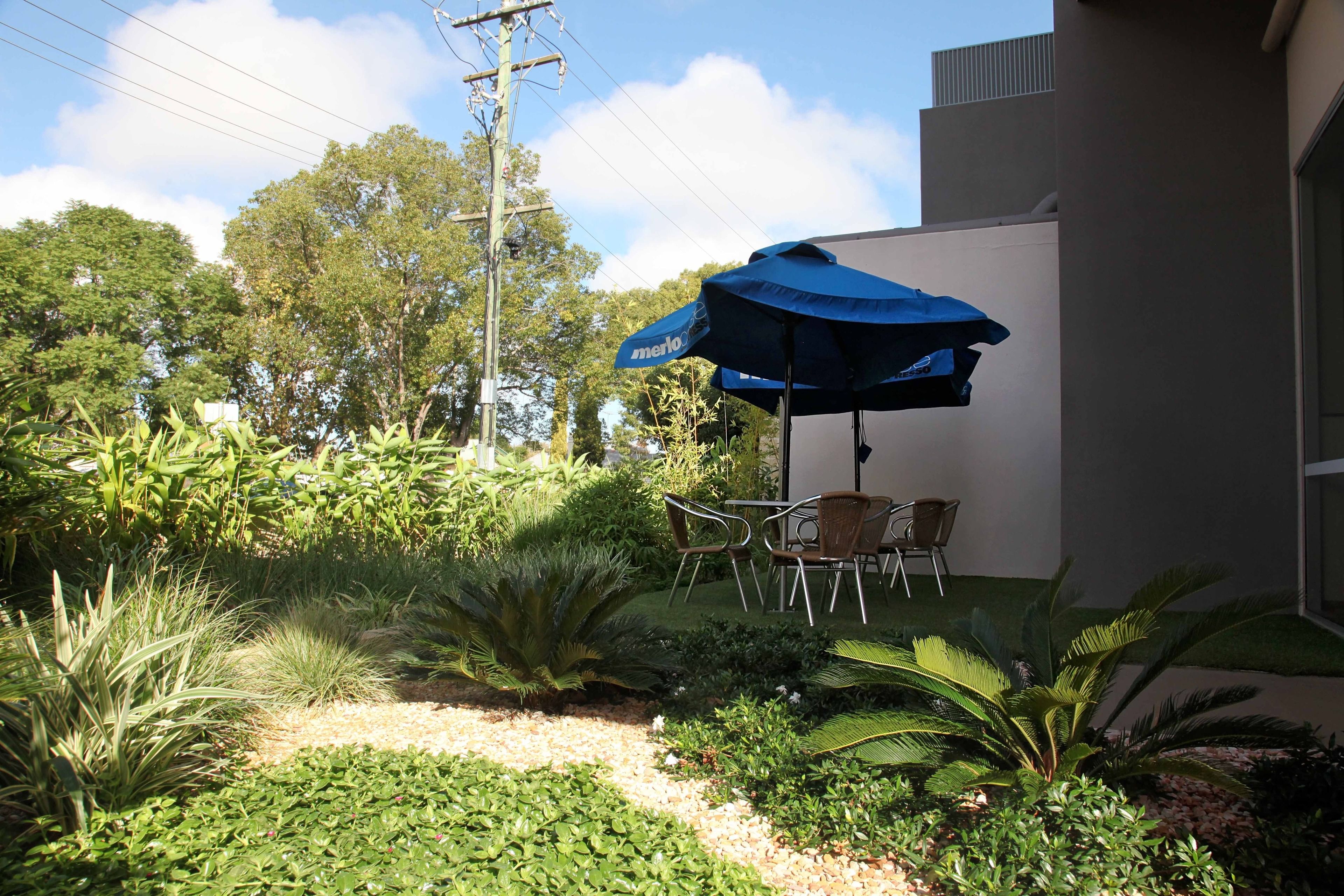 A patio with a blue umbrella, outdoor seating, and lush greenery.