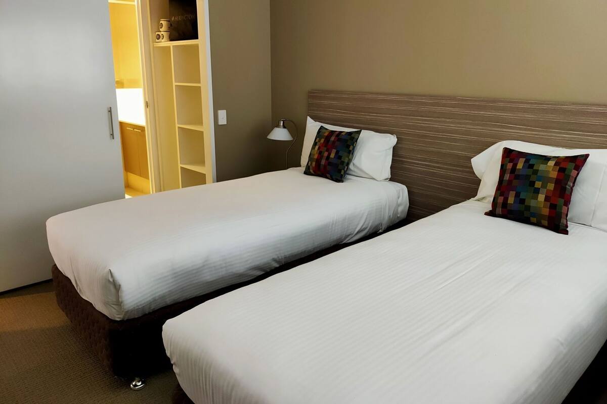 A hotel room with two beds, a wardrobe, and a bedside lamp.