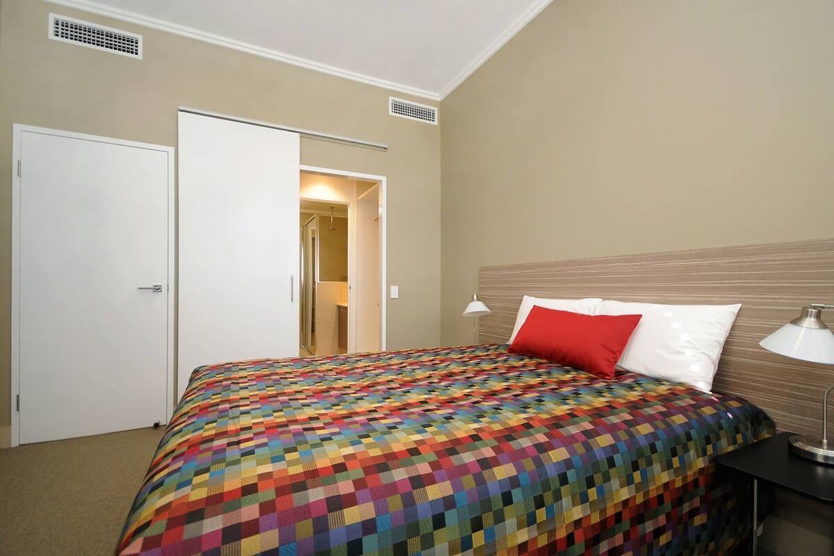 A hotel room with a bed, a nightstand, a lamp, a door, and a closet.