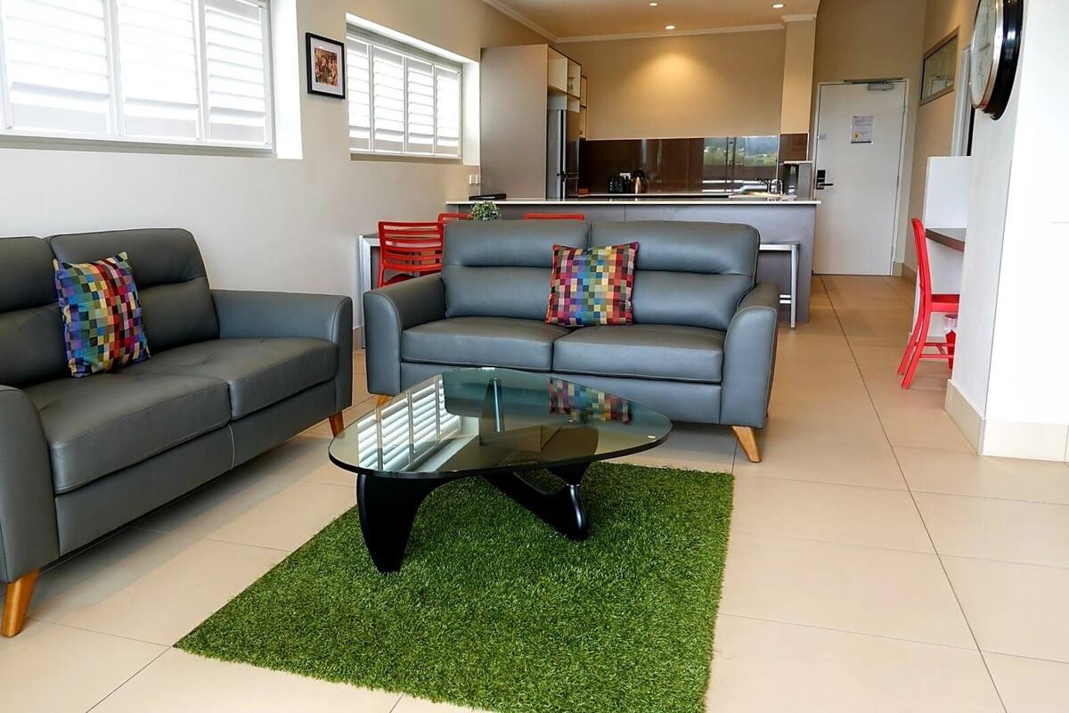 A modern living room with two grey sofas, a glass coffee table, and a green rug.