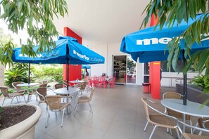 A café area with tables and chairs, blue umbrellas, and red pillars. - Laguna Apartments (Toowoomba)