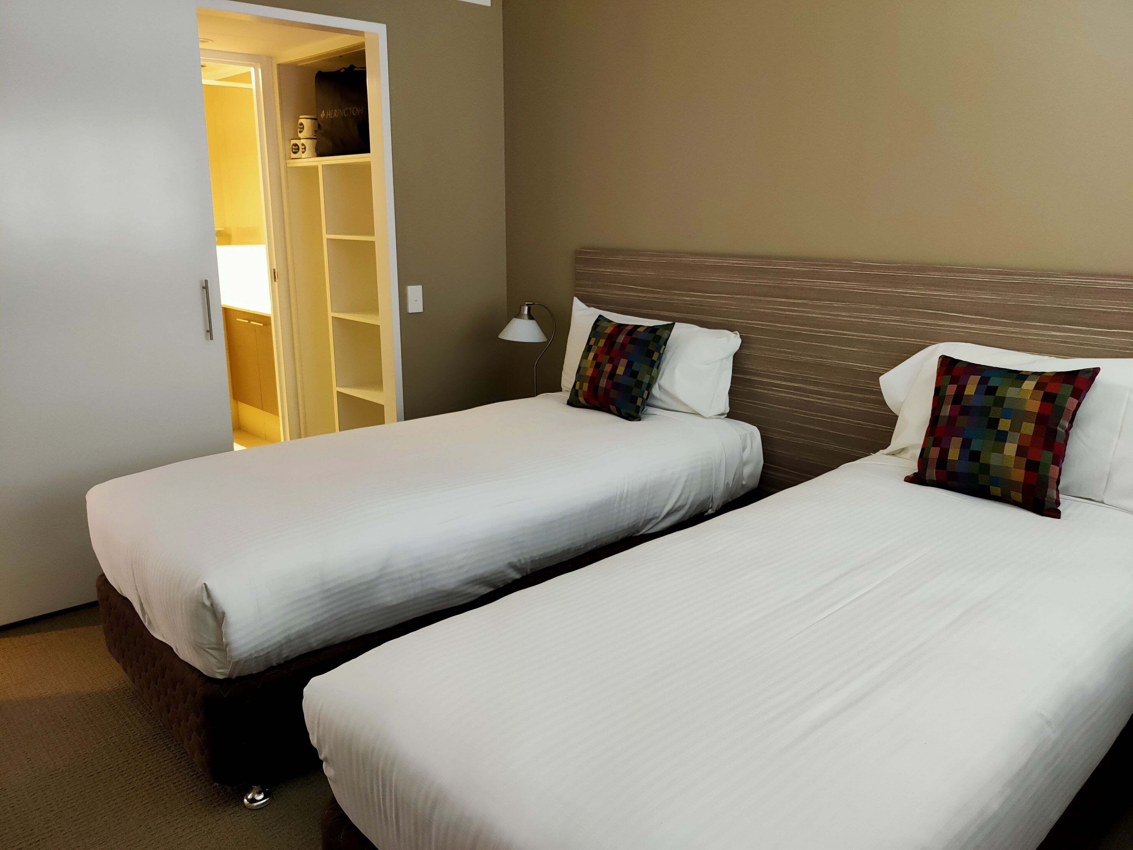 A hotel room with two single beds, a wardrobe, and a bedside lamp.