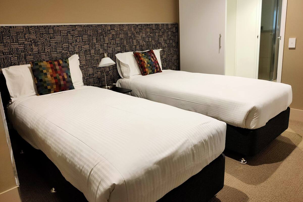 Two single beds with white linens, a patterned headboard, and a nightstand with a lamp.