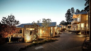 A row of modern, multi-story buildings with stone facades and large windows, connected by a gravel pathway. - Hepburn Spa Retreat (Hepburn Springs)
