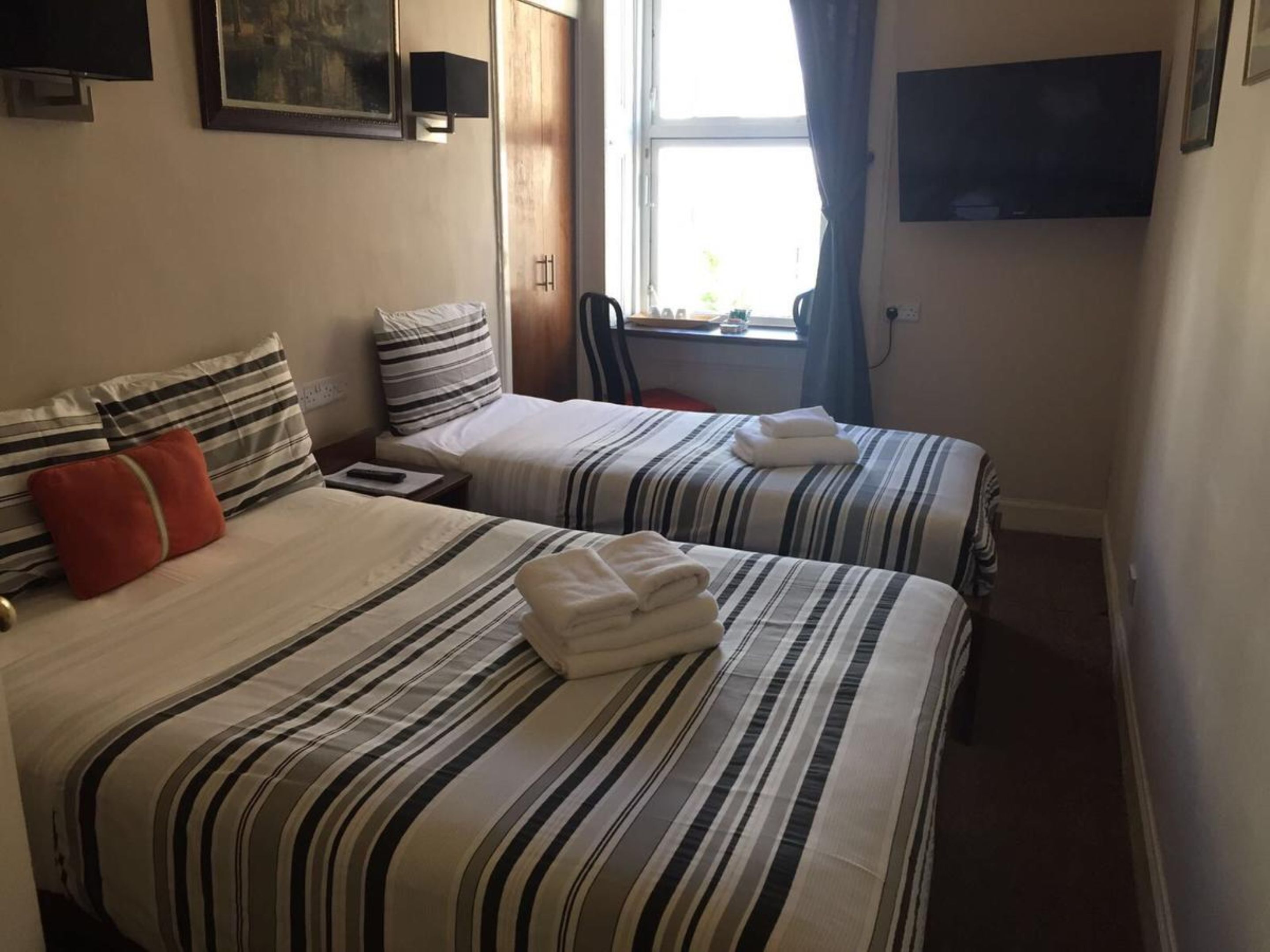 Ein Hotelzimmer mit zwei Betten, gestreifter Bettwäsche, einem Fernseher und einem Fenster mit Vorhängen.