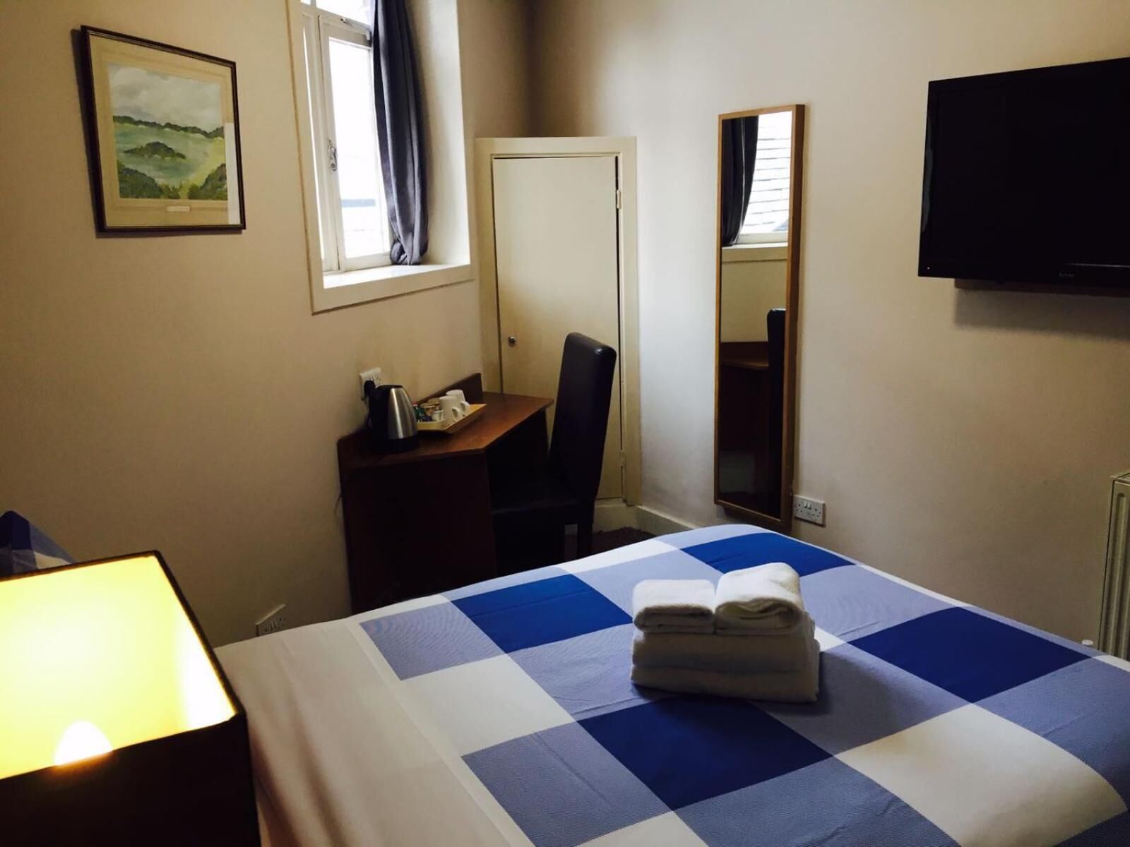 A hotel room with a bed, a desk, a chair, a television, and a window with curtains.