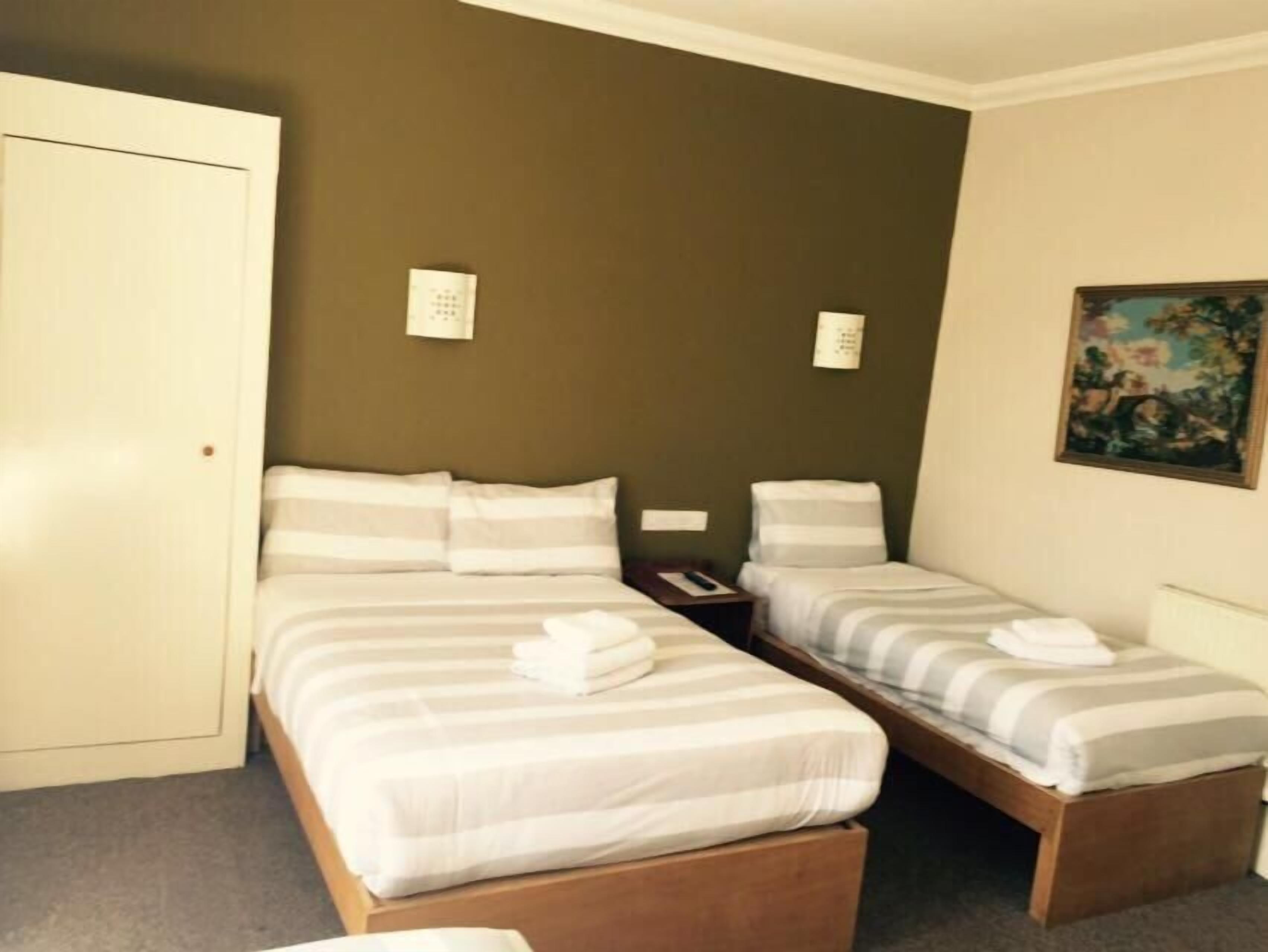 A hotel room with two beds, a wardrobe, and a painting on the wall.