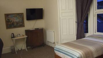 A bedroom with a bed, a TV mounted on the wall, a desk, and a radiator.