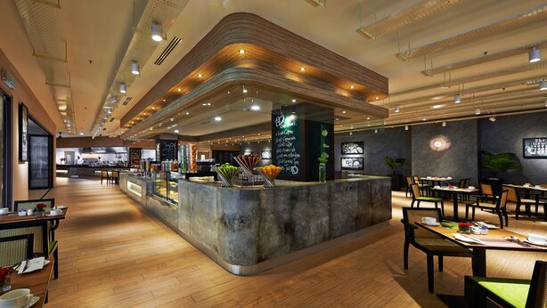 A modern restaurant with a central counter, wooden flooring, and a mix of seating arrangements including tables and booths. - Premiera Hotel Kuala Lumpur (Kuala Lumpur)