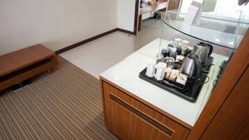 A hotel room with a wooden cabinet, a glass table with a tray of breakfast items, and a small wooden bench.