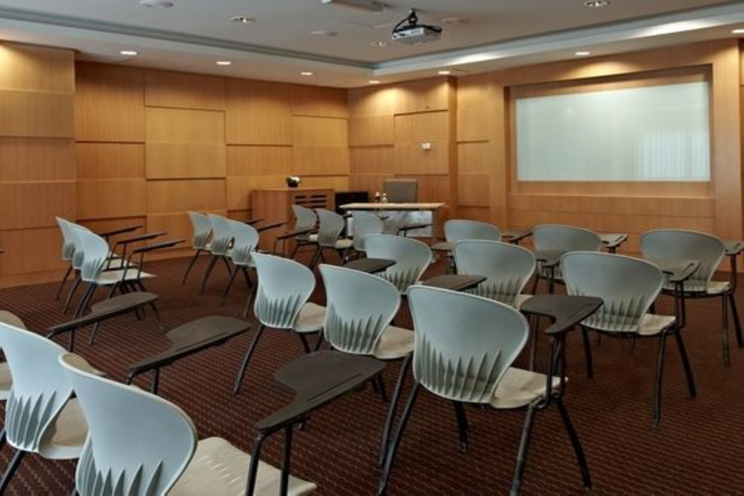 Un salón de conferencias con filas de sillas, una pantalla de proyector y un atril.