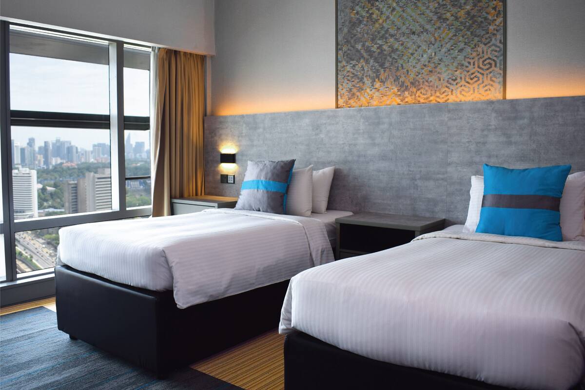 Une chambre d’hôtel avec deux lits, une vue sur la ville, un élément décoratif mural et une table de chevet avec une lampe.