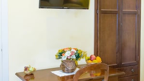 A dining area with a wooden table, a chair with a blue cushion, a television mounted on the wall, and a wooden cabinet. - Bed & Breakfast Armonia (Syracuse)