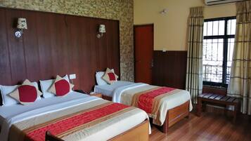 Quarto de hotel com duas camas, cabeceira de madeira, um banco de madeira, aparelho de ar condicionado e uma janela com cortinas.
