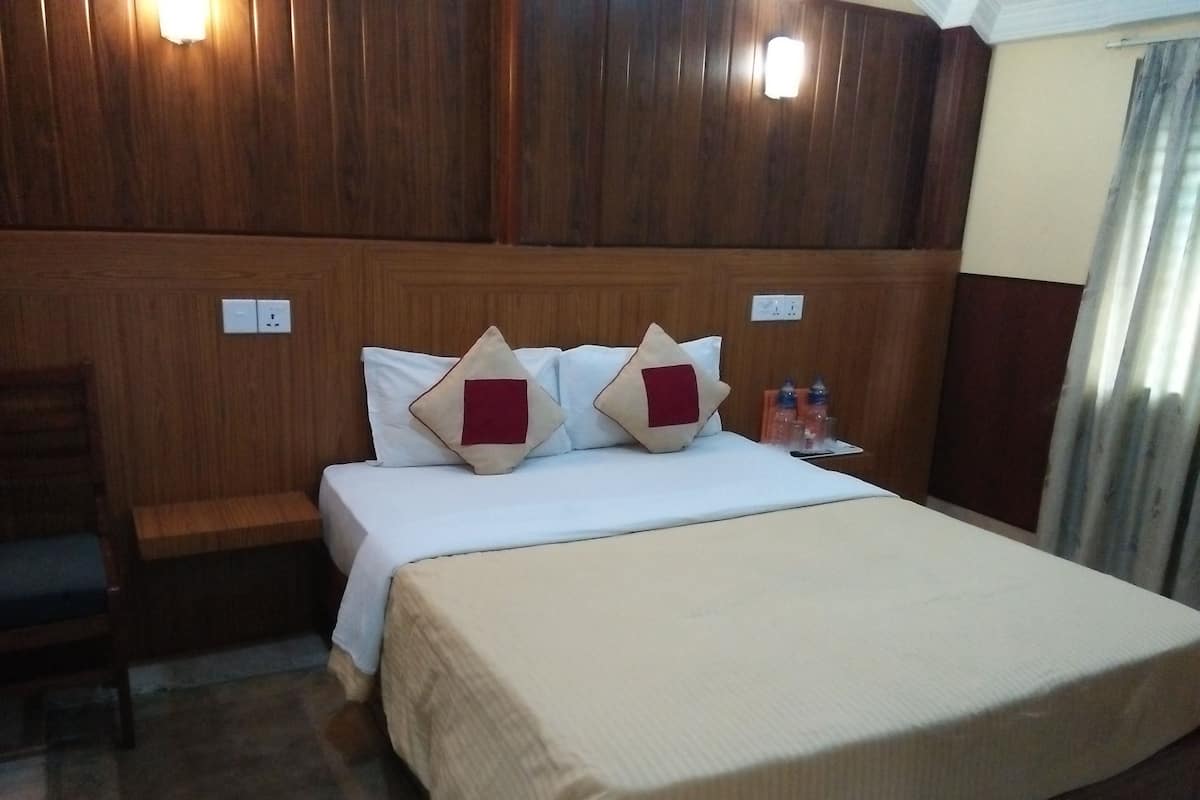 A hotel room with a wooden headboard, a bed with white bedding and two decorative pillows, a bedside table with a water bottle, and a power outlet.