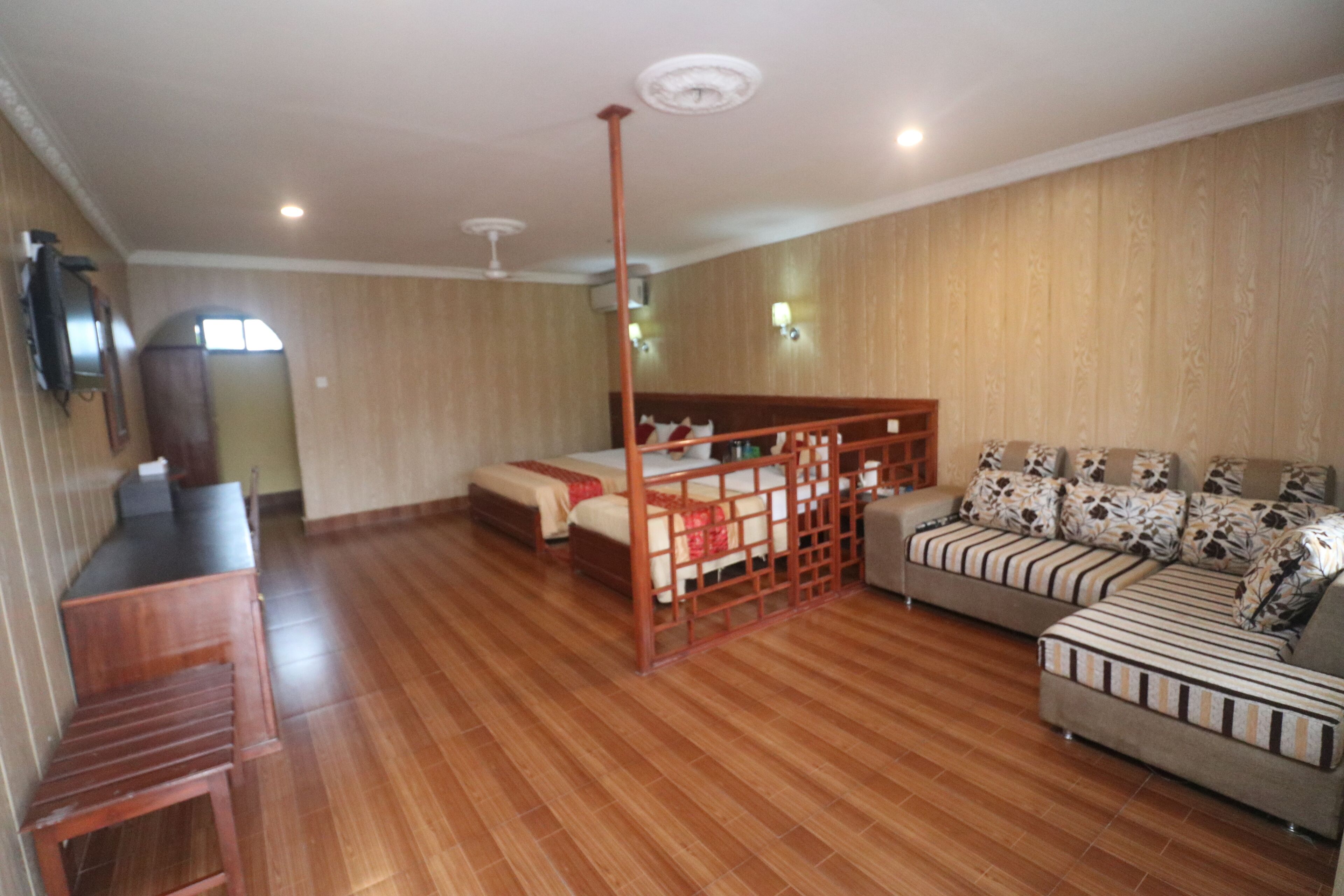 A spacious room with a wooden floor, a bed with a wooden headboard, a sofa, and a small wooden table.