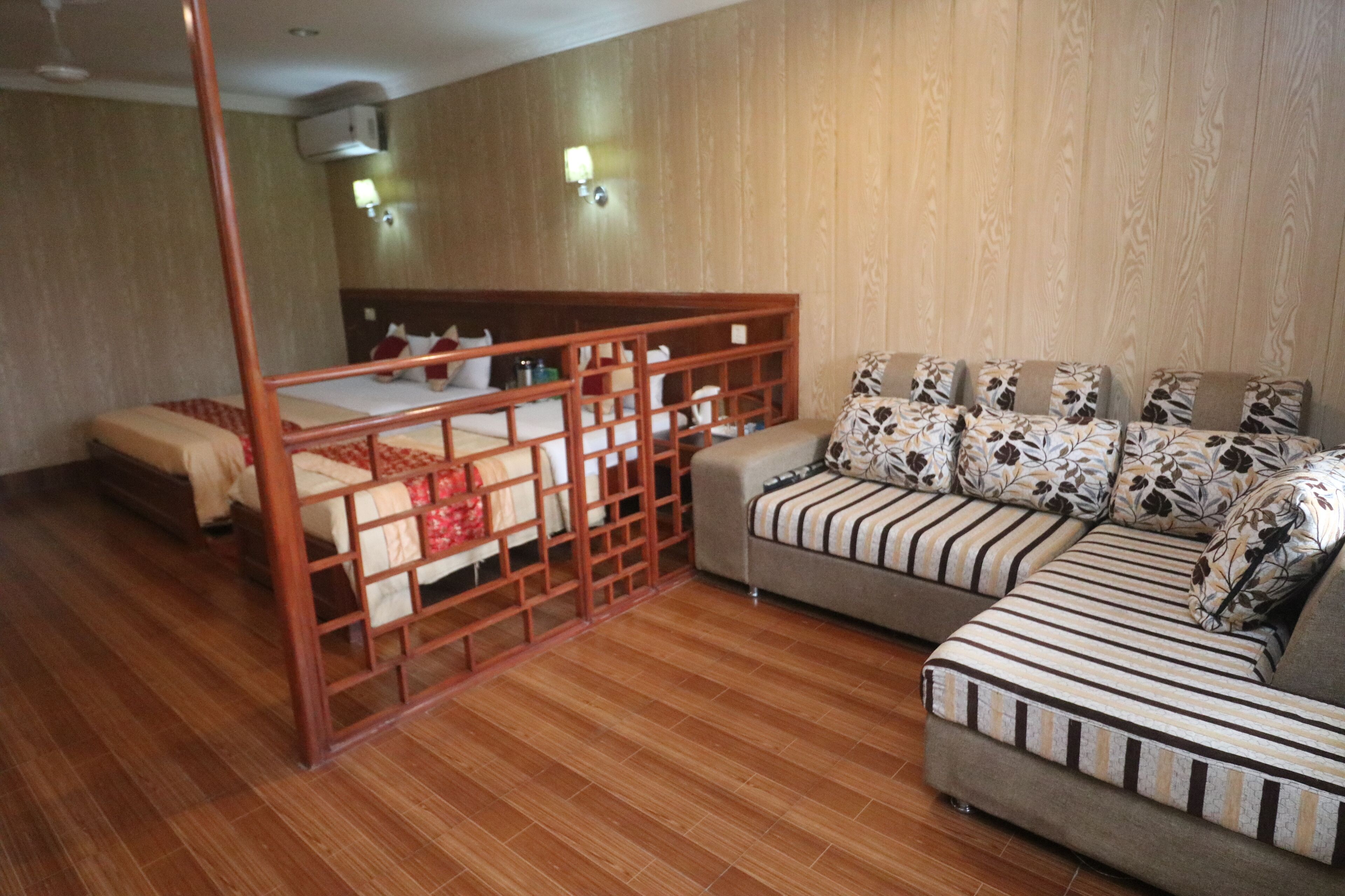 Habitación de hotel con piso de madera, cama con cabecera de madera, sofá con cojines estampados y una mesita.
